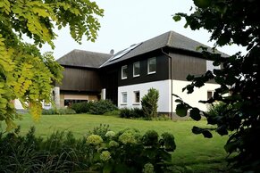 Ein zweistöckiges Haus mit schwarz-weißer Fassade liegt inmitten eines üppigen Gartens, umrahmt von Bäumen und Sträuchern.