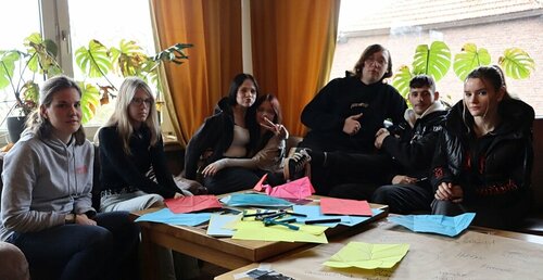 Sechs Start-off-Jugendliche versammeln sich in einem Wohnzimmer um einen Tisch und üben eine kreative Tätigkeit aus.